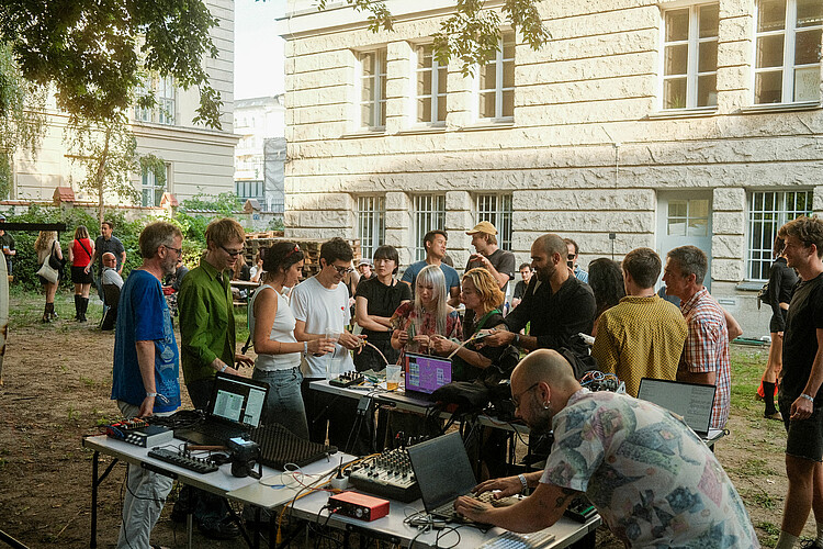 Viele Personen stehen im Garten des Medienhauses. Im Vordergrund ist ein Tisch mit Mischpulten und Kabeln zu sehen.